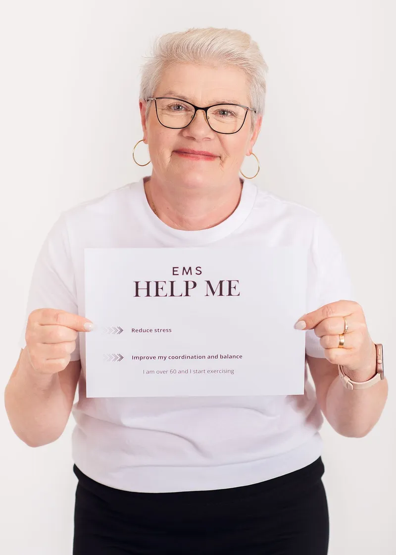 A smiling client with short grey hair holds a card headed EMS Help Me