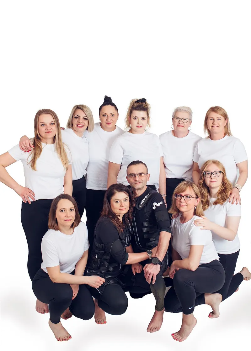 Anna and Rafal in black EMS suits, kneeling among Smart Body Studio clients in white T-shirts
